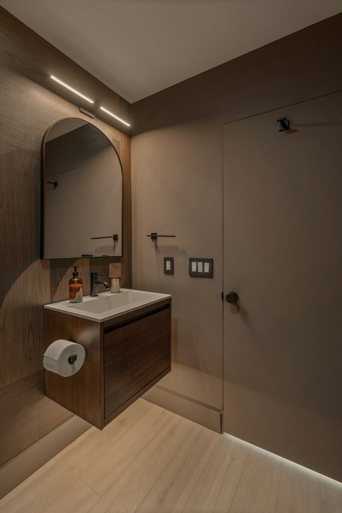 Modernes Bad mit Holz-Vanity, Bogen-Spiegel und warmer Indirekt-Beleuchtung